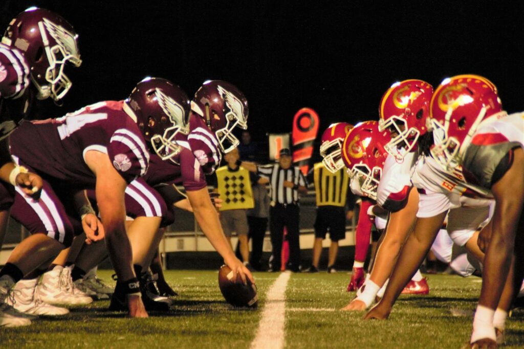 Football teams lined up at the line of scrimmage under stadium lights